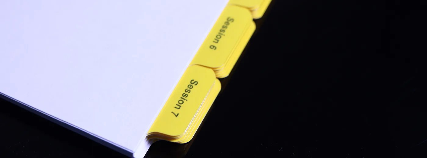 Macro view of Mylar film reinforcing the edge of a printed index tab — Mylar reinforcing performed in-house at Anselmo Die & Index
